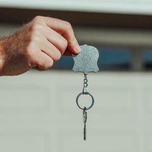 A close-up image of a hand holding a key with keychain outdoors, symbolizing new home or rental purchase.