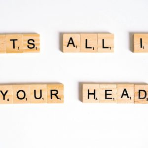 Wooden Scrabble tiles arranged to spell 'ITS ALL IN YOUR HEAD' on a white background.