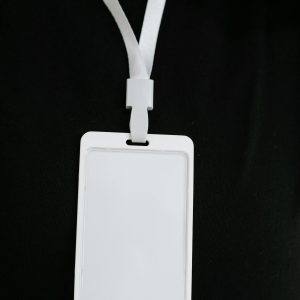 Plastic name tag with white ribbon and blank paper hanging on black background