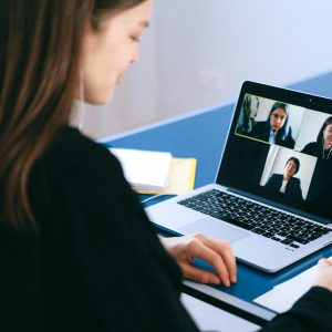 A woman engaging in a video conference using a laptop at home, taking notes.